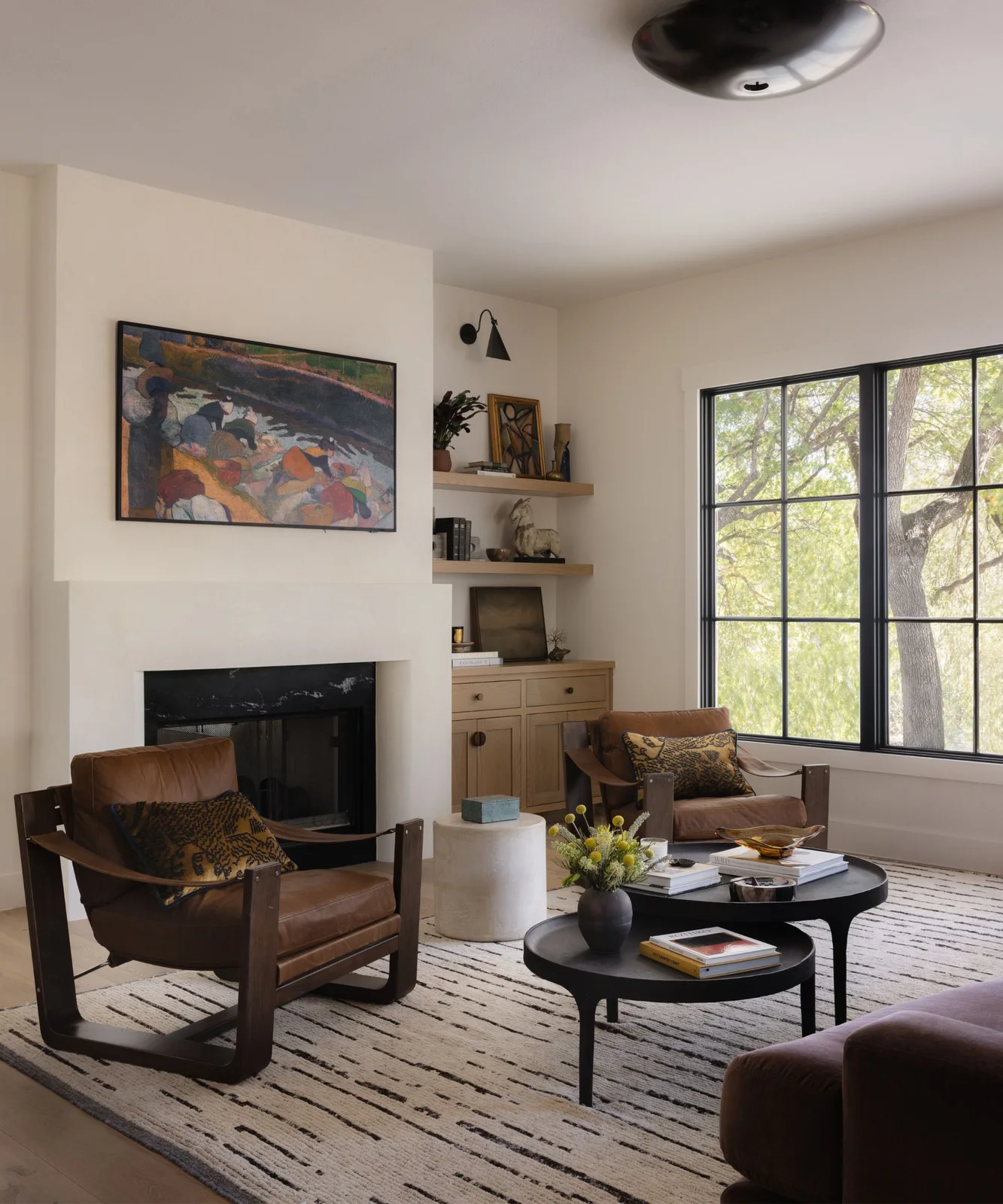 Brown cushioned chairs with open timber frames face low black tables beside a pale fireplace and timber alcove shelves.