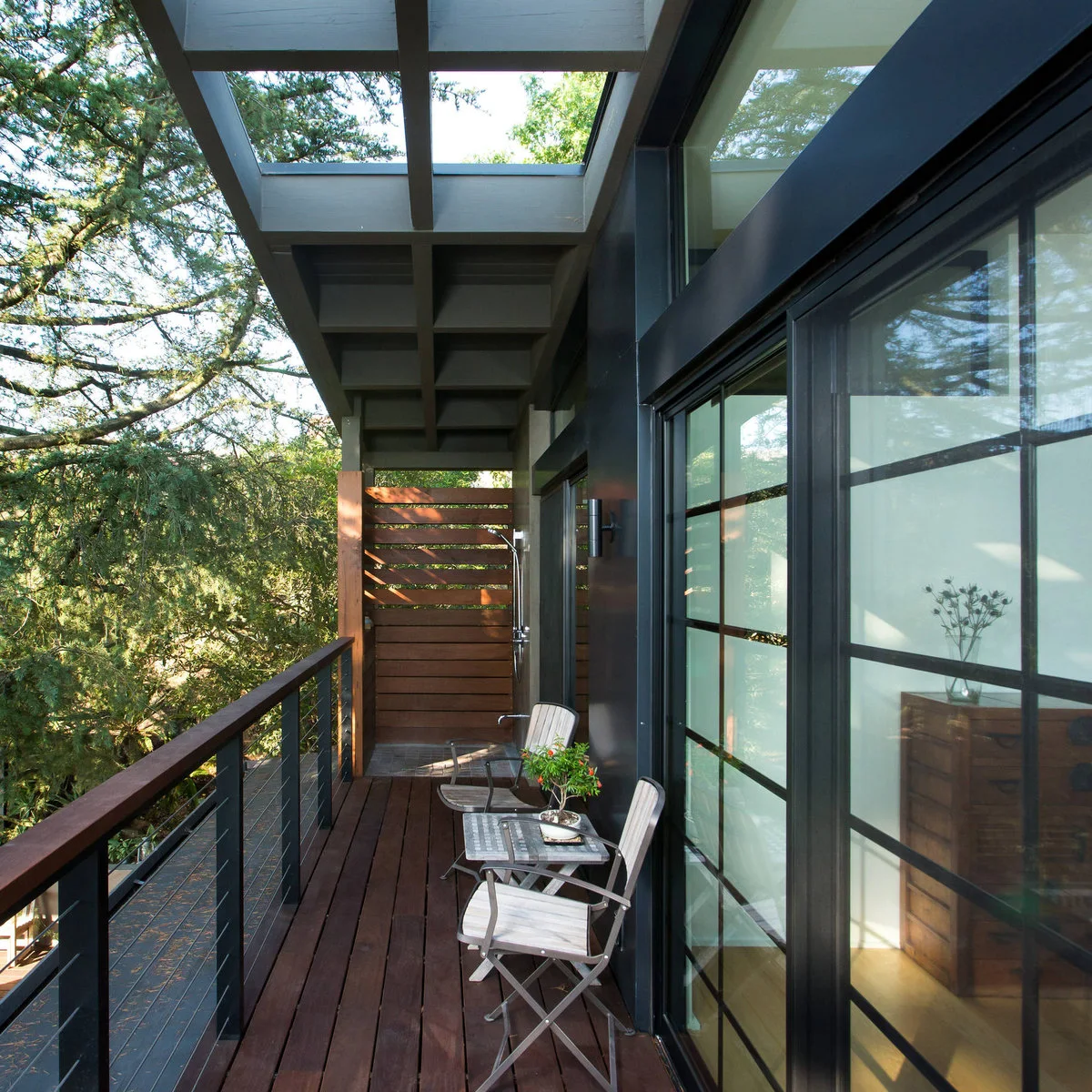 A timber end screen has a solid lower half and spaced upper slats beside balcony chairs