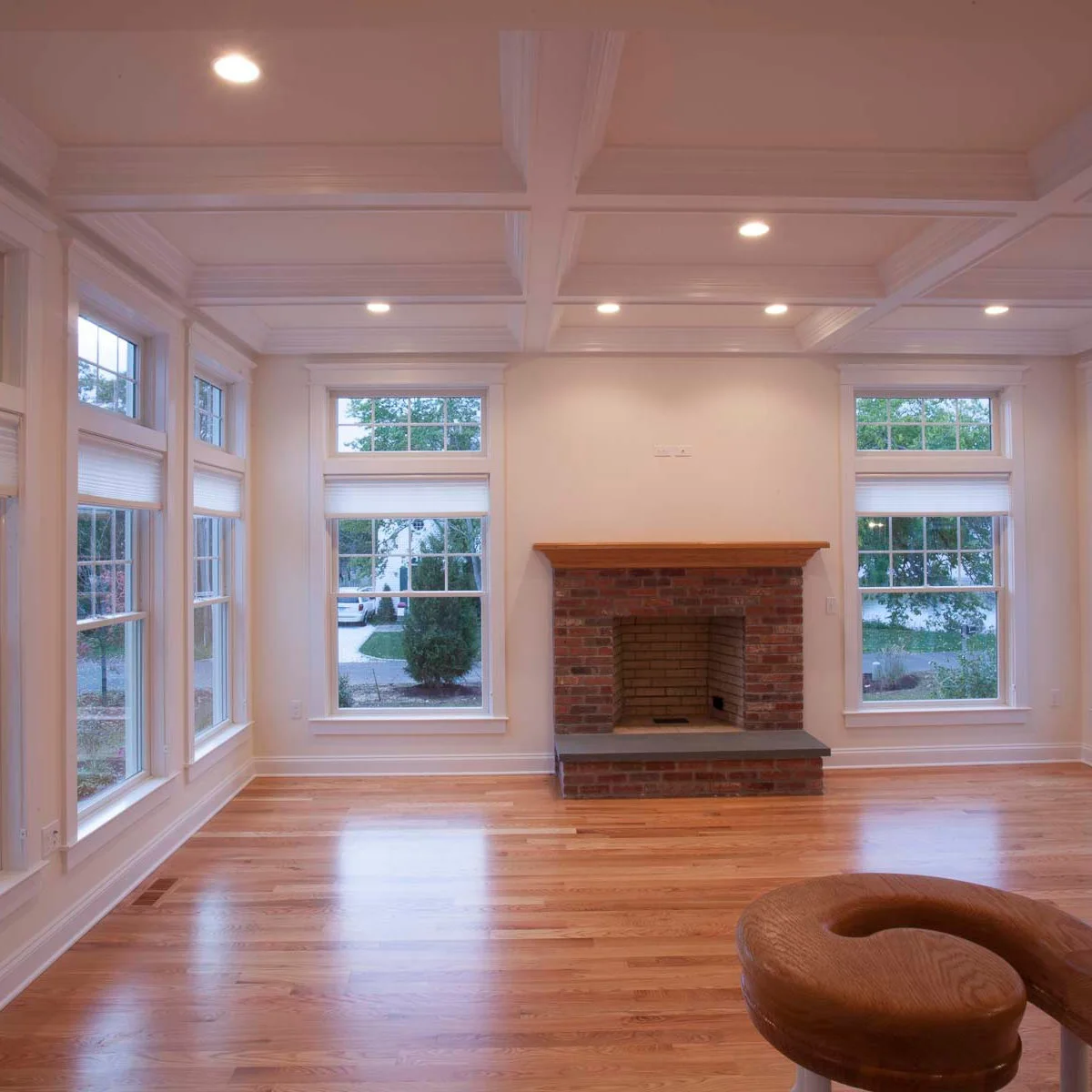 A compact red brick fireplace with a wood mantel and dark hearth top sits between tall white-trimmed windows in a pale room.