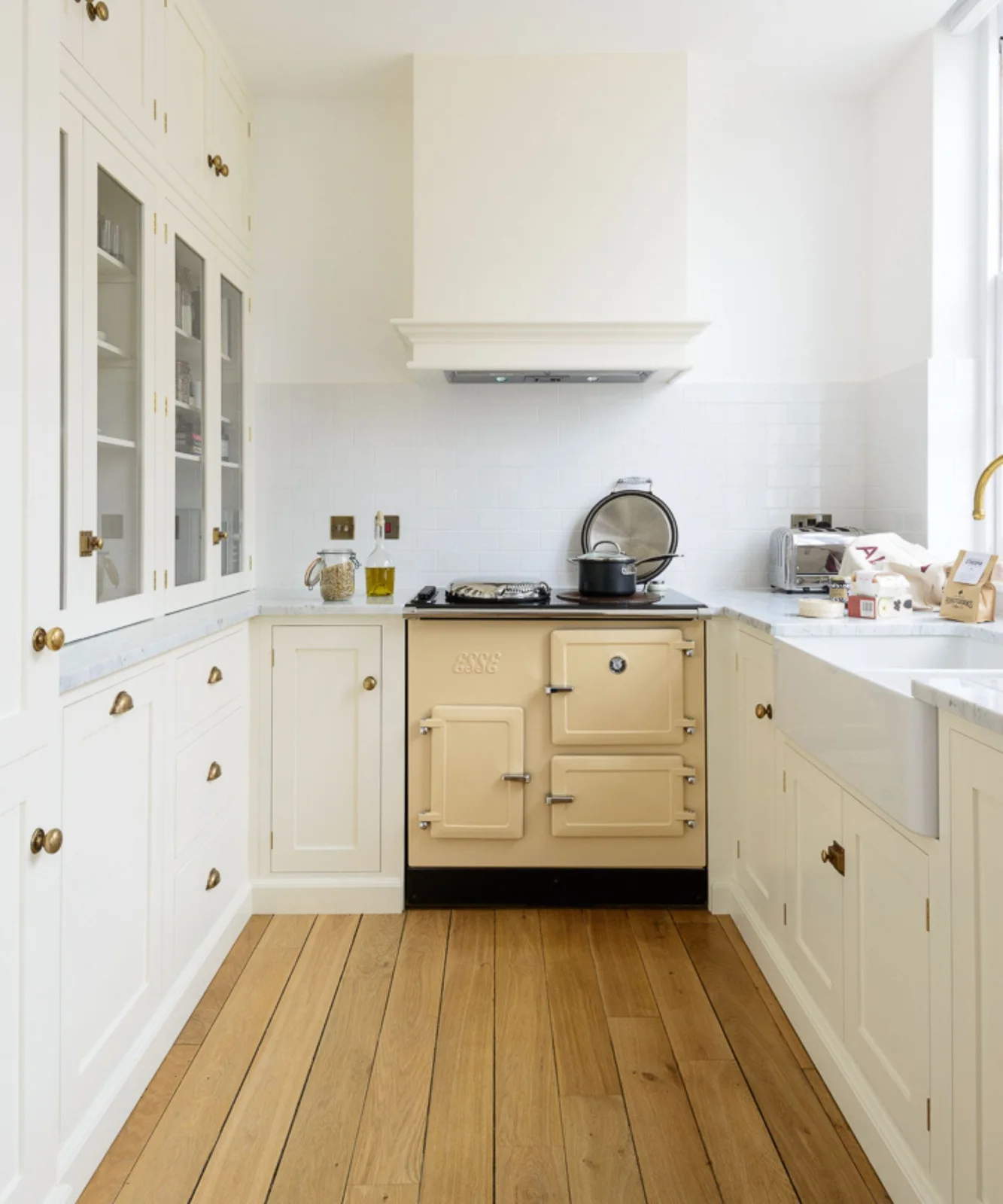 Soft white framed cupboards surround a cream range with glass-front storage to one side and a sink to the other.
