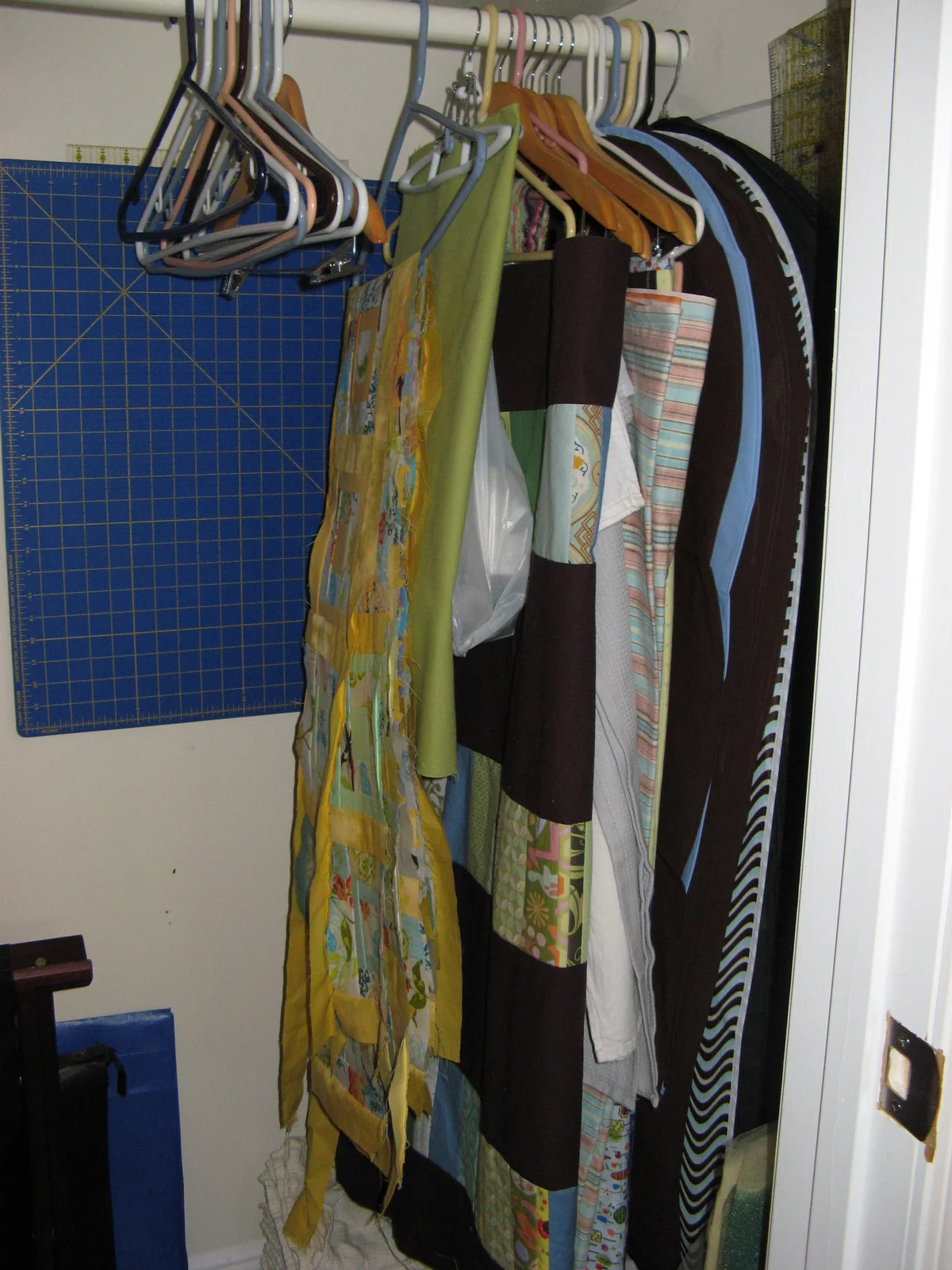 Quilts and fabric pieces hang inside a closet beside a large blue cutting mat and measuring tools on the side wall.