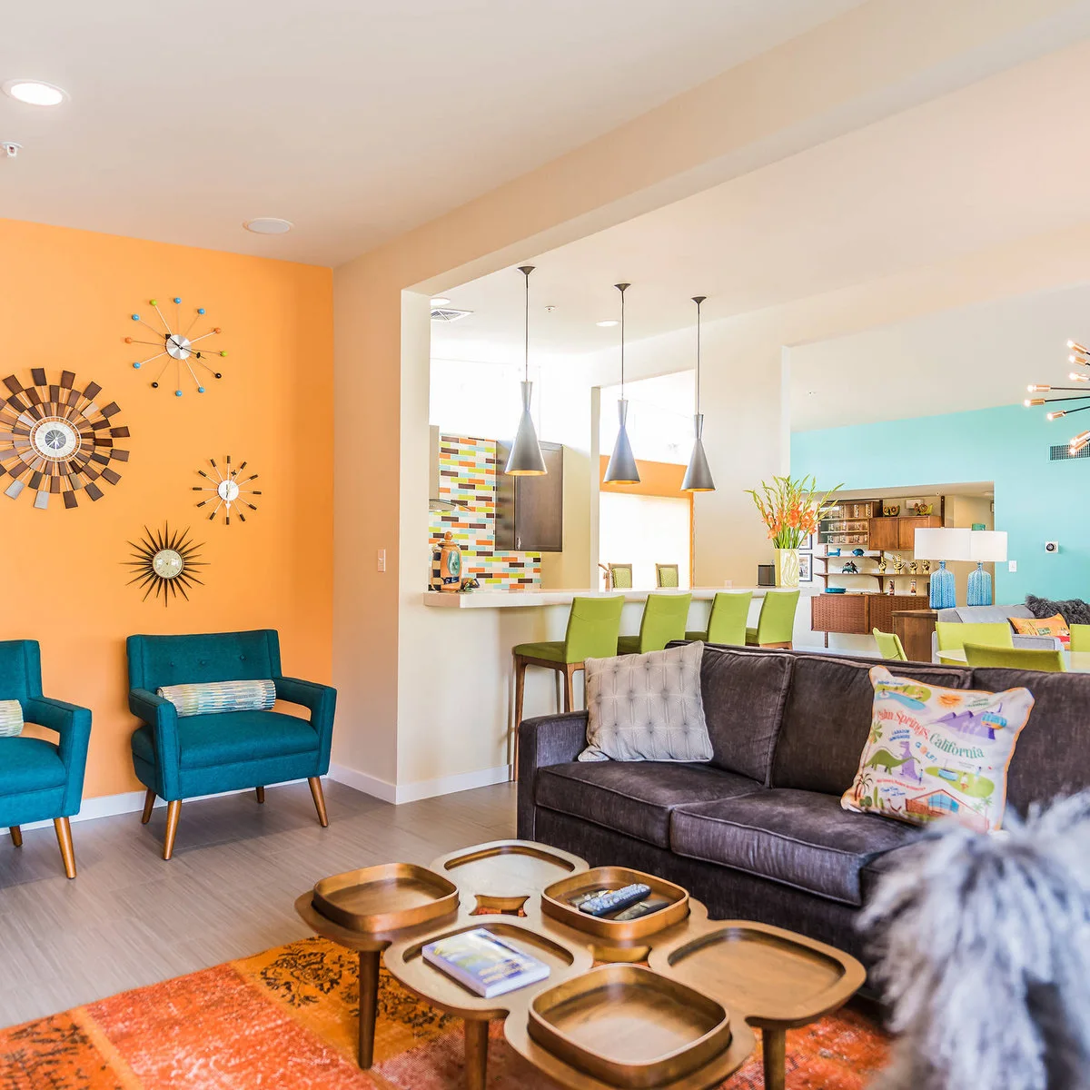 Charcoal gray sofa faces teal chairs beside an orange wall, with an orange rug in the seating area.