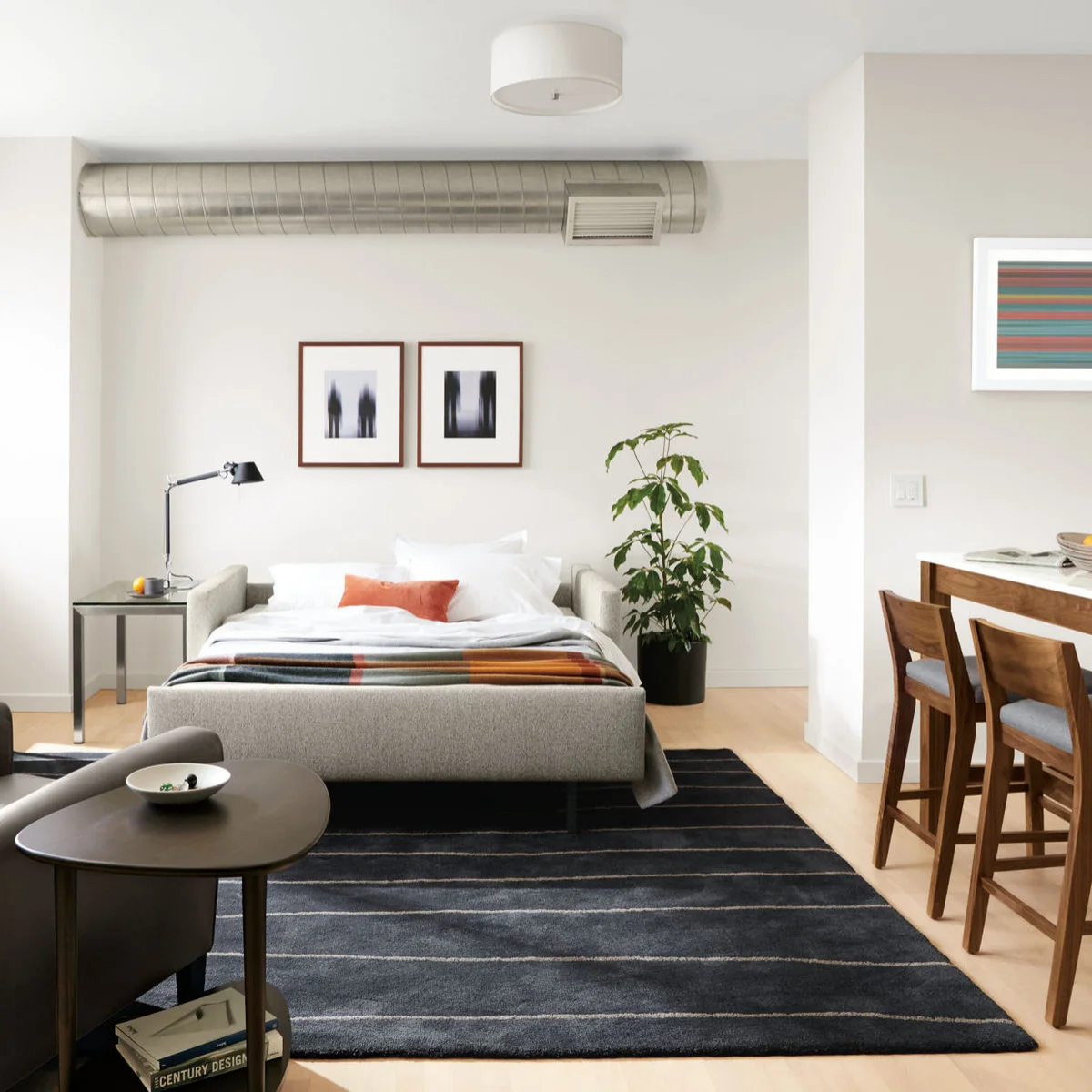 Open gray sofa bed with white bedding, an orange cushion and an adjustable lamp on a side table