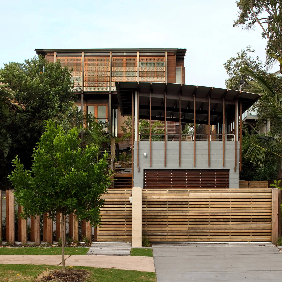 Driveway entering through a horizontal timber gate beside a smaller pedestrian gate, tree and planted boundary.
