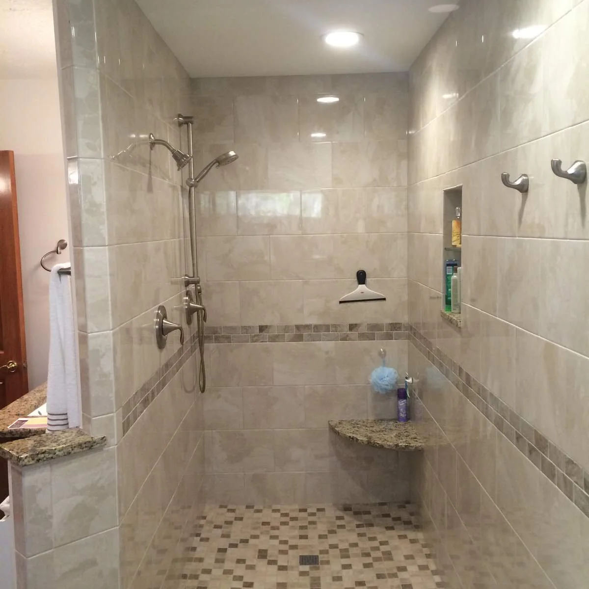 Beige tiled shower with a small triangular corner seat and tall bottle niche