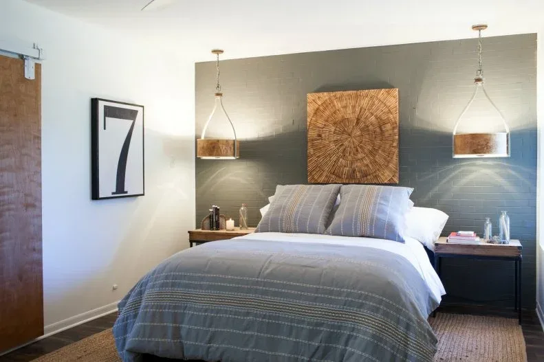 Muted green bedroom wall with a large warm woven accent, pendant shades and pale gray bedding
