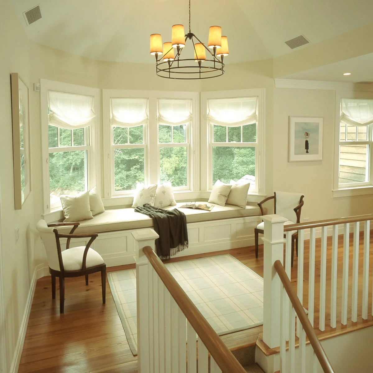 A long white bay-window seat with pale cushions and two wooden chairs on a stair landing.