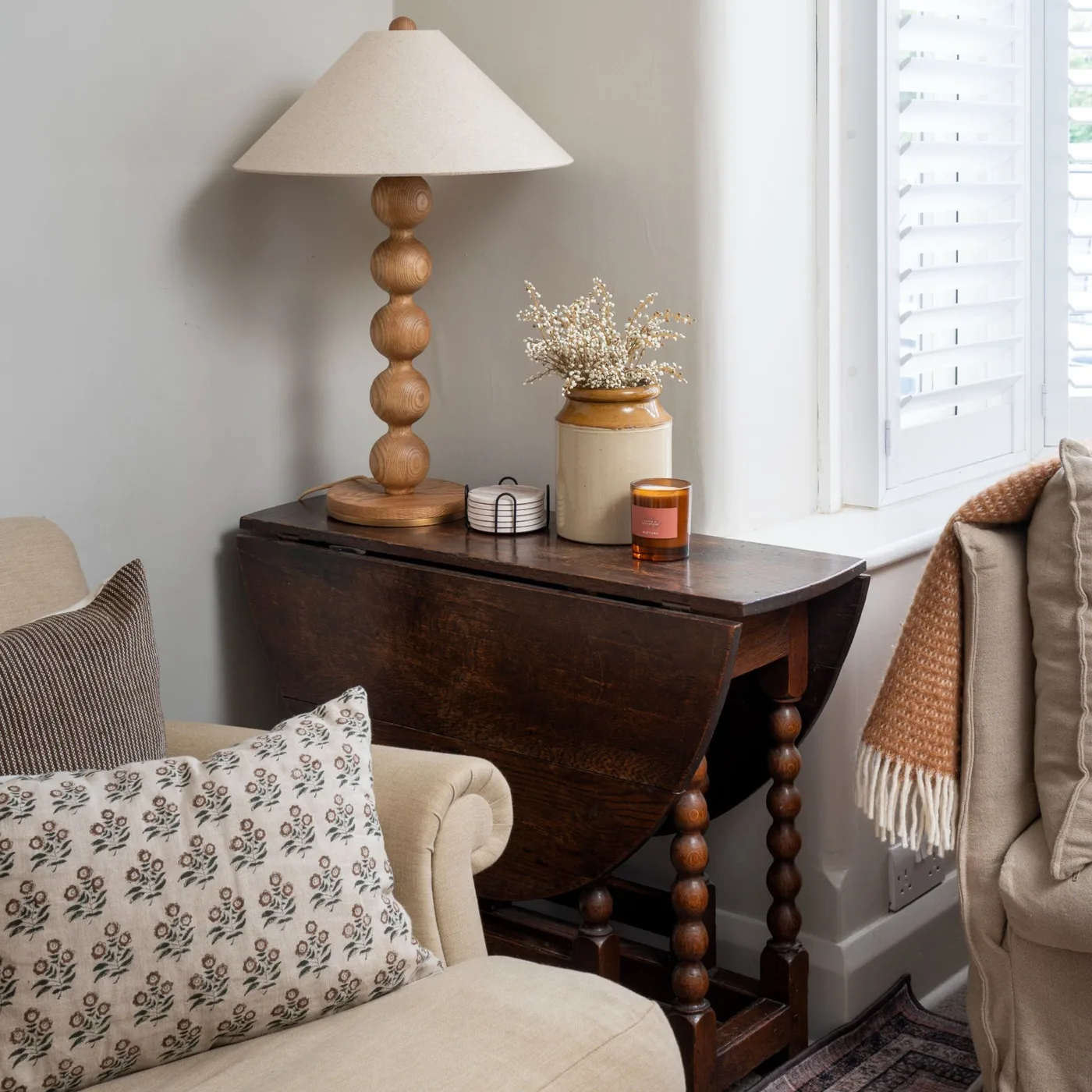 Dark wood drop-leaf side table between pale seats with a rounded wood lamp base and simple light shade