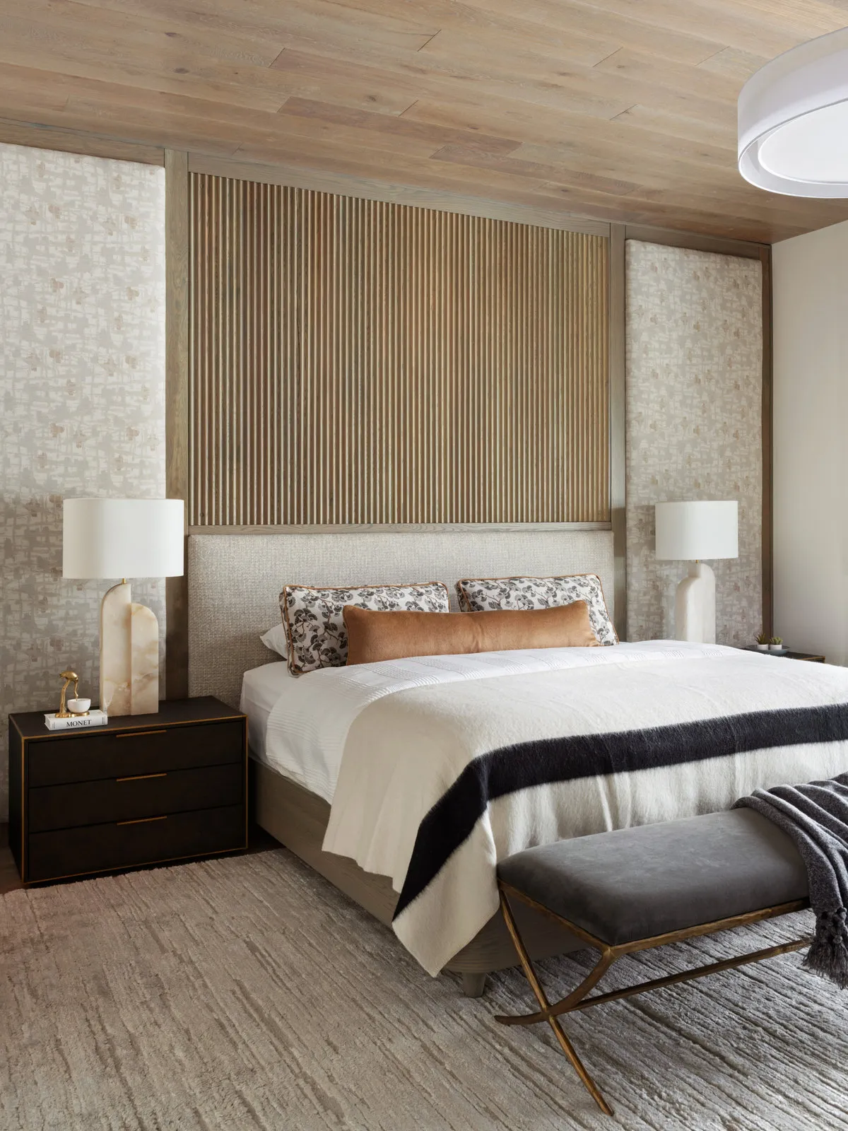 A pale bed and dark bench sit beneath timber ceiling and wall details.