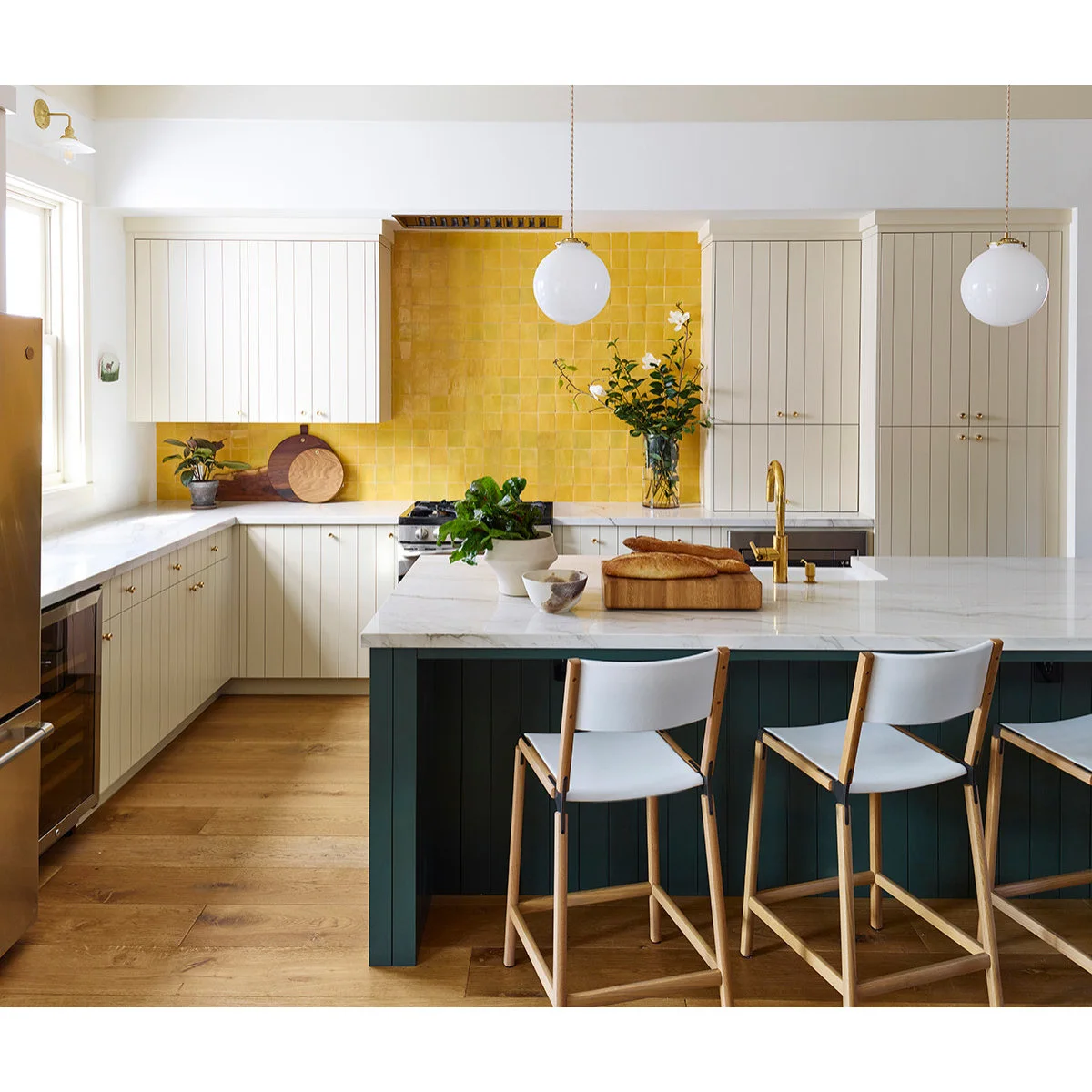 Pale kitchen cabinets with a yellow square-tile backsplash, dark green island and globe pendants