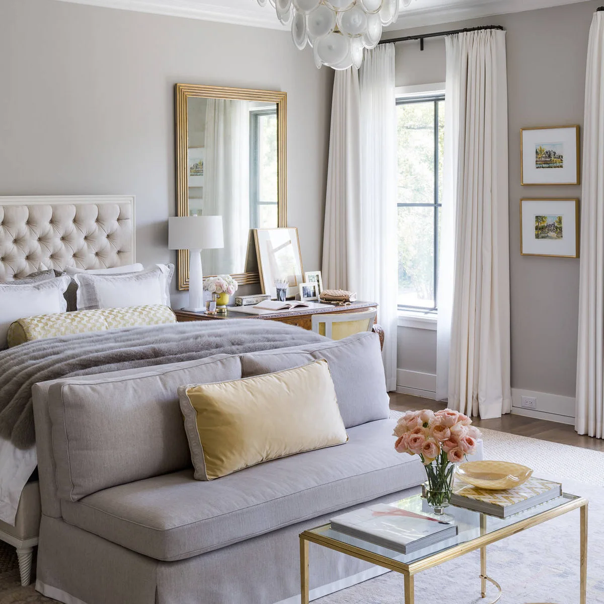 Bedroom with a cream headboard, pale butter-yellow cushions and bolster, gray seating and a gold-framed mirror