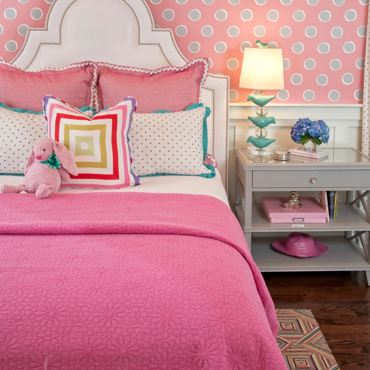 Pink bed with gray dotted wallpaper, dotted pillows and a gray bedside table