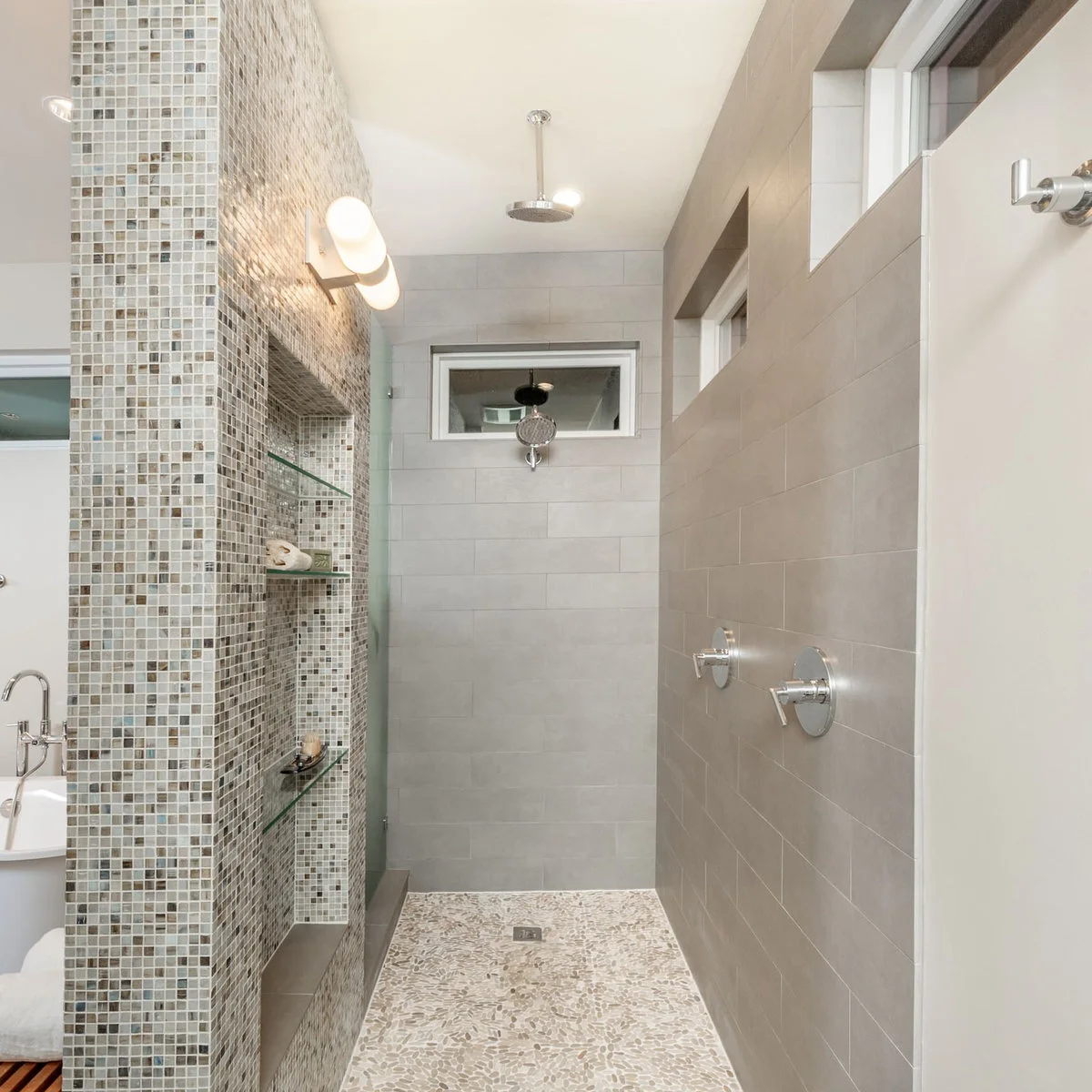 Mosaic-clad shower divider with recessed glass shelves beside pale large wall tiles