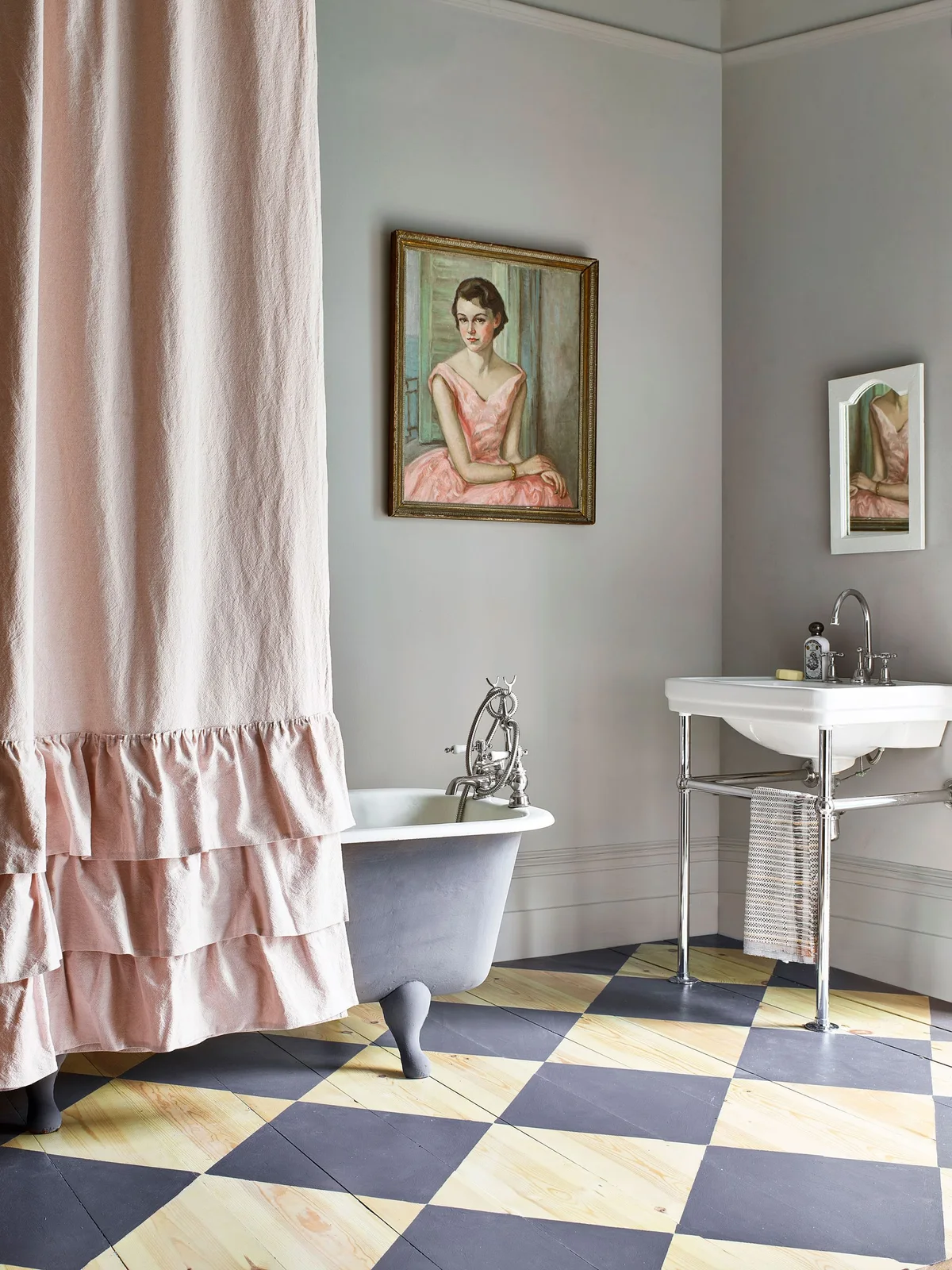 A gray traditional tub and pink curtain above diagonally checked painted wooden floorboards