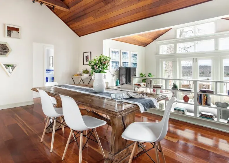 Low white open shelving with a metal rail beside a raised dining area and a long wood table