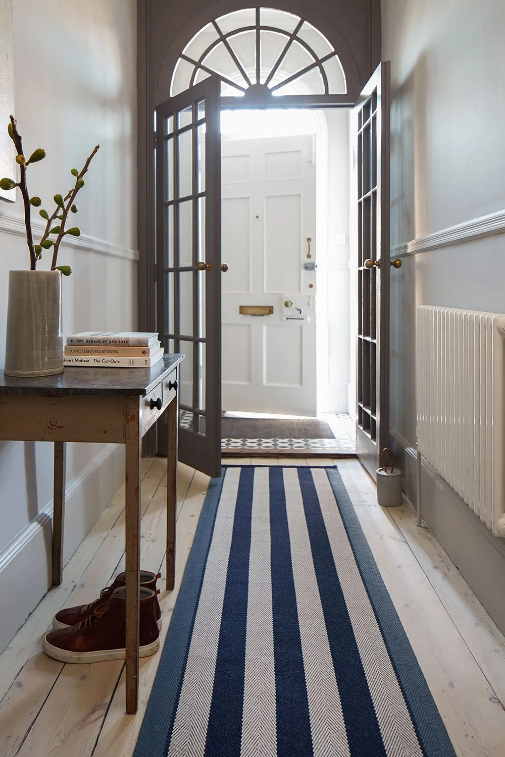 Blue and pale striped runner on painted floorboards beside a wood table, dark glazed doors and white front door