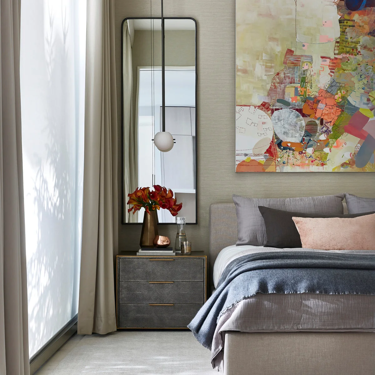A gray bedside chest and pendant beside a pale bed, with colorful abstract artwork above the headboard.