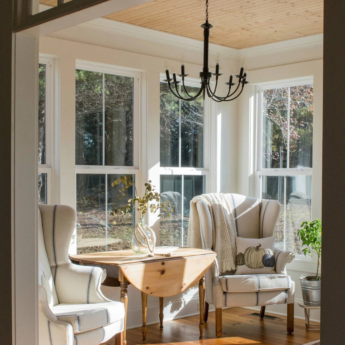Light plank ceiling over a small wood dining table and two pale upholstered chairs