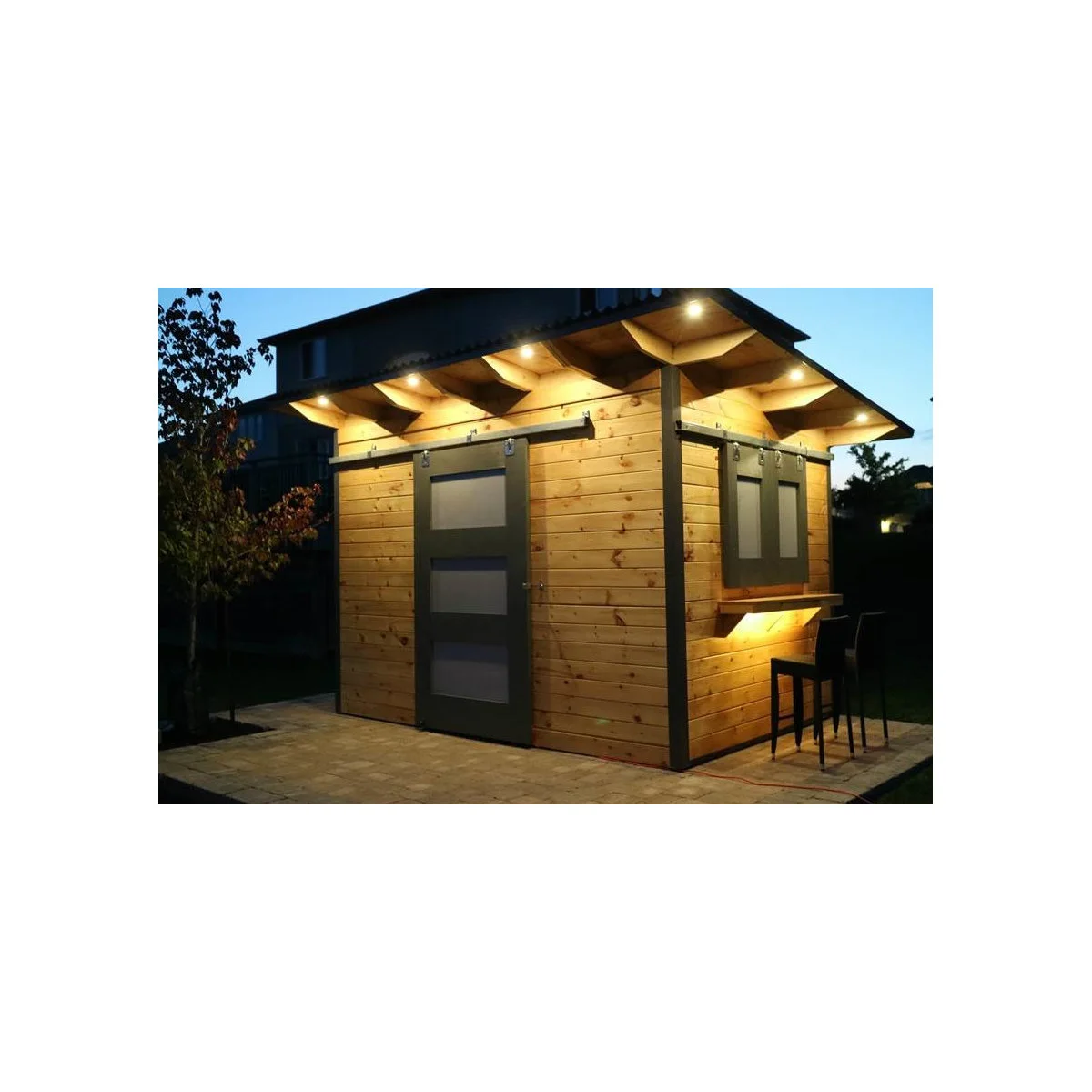 Wood bar shed with grey sliding shutters, a side counter and small lights beneath the eaves
