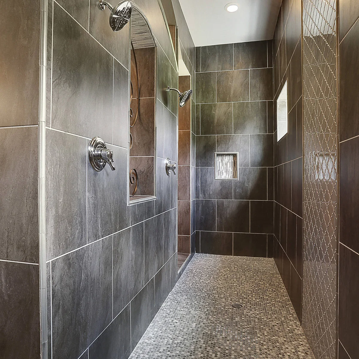 Long dark tiled shower with small floor mosaics and a narrow decorative wall strip