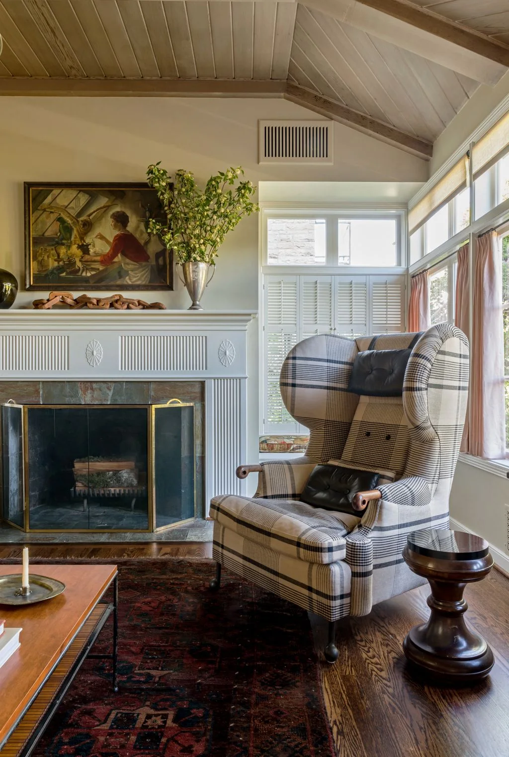 Tall checked wing chair beside a white fireplace, dark wood side table and patterned rug