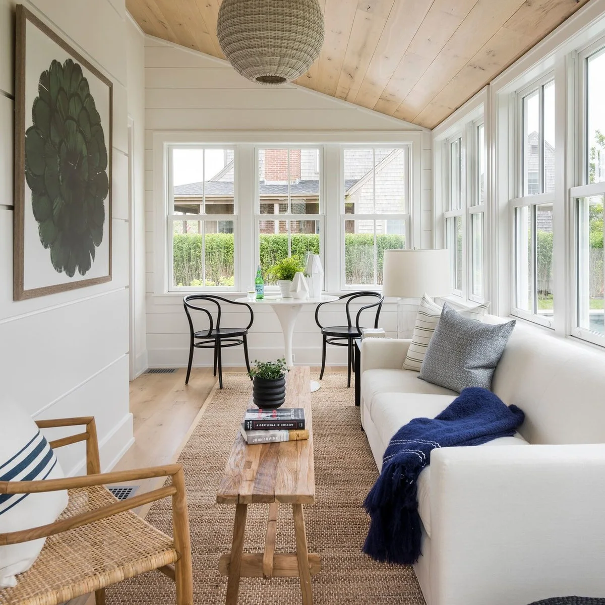 Pale wood plank ceiling above a white sofa and round table in a small glazed room