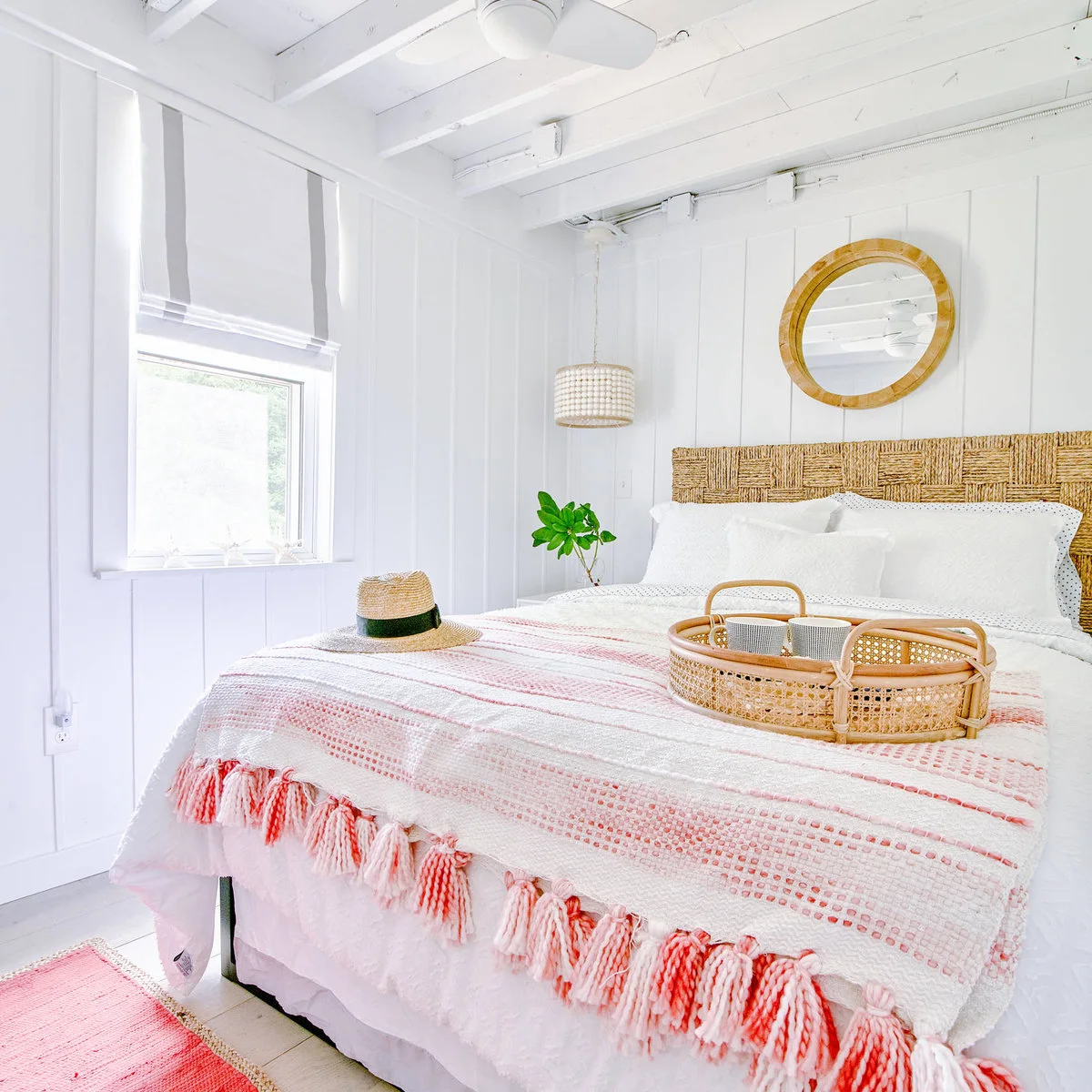 White paneled bedroom with woven headboard, round mirror and pink-striped fringed throw