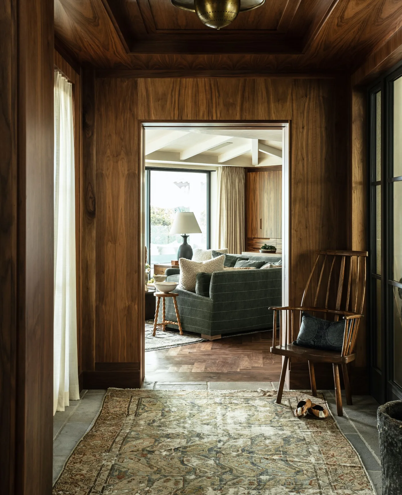 A wooden spindle chair and patterned rug in a dark timber lined entrance opening to a living room