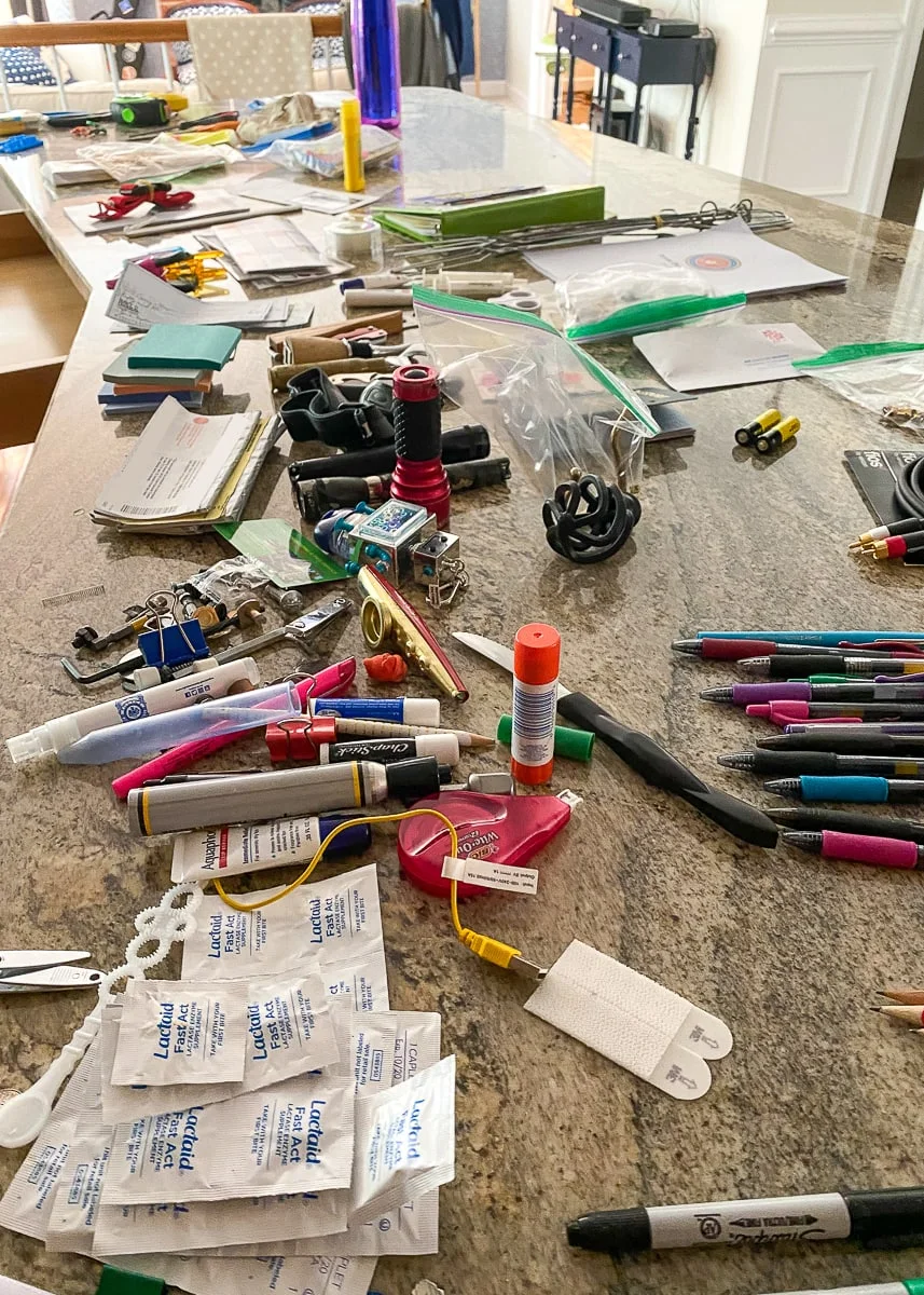 Household drawer contents sorted across a kitchen counter, including pens, tools, tape and paper