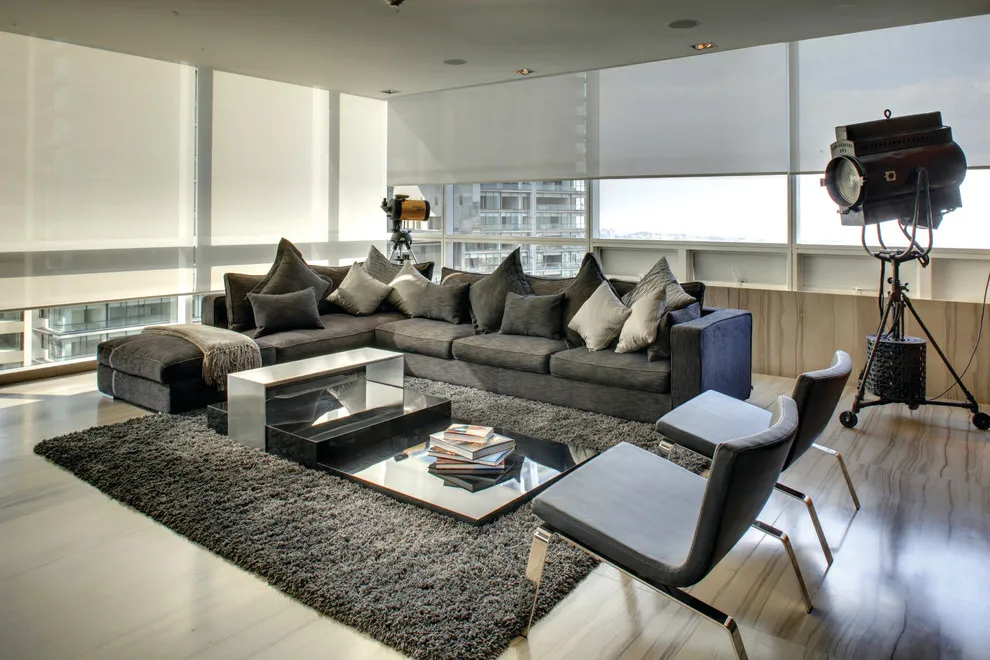 A dark gray modular sofa fills the center of a bright room with broad windows and a deep textured rug