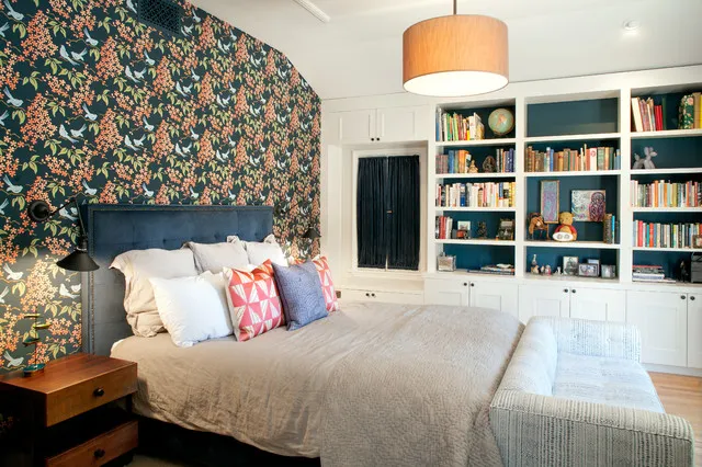 Deep blue floral wallpaper sits behind a dark upholstered headboard with pale bedding and white bookcases beside it.