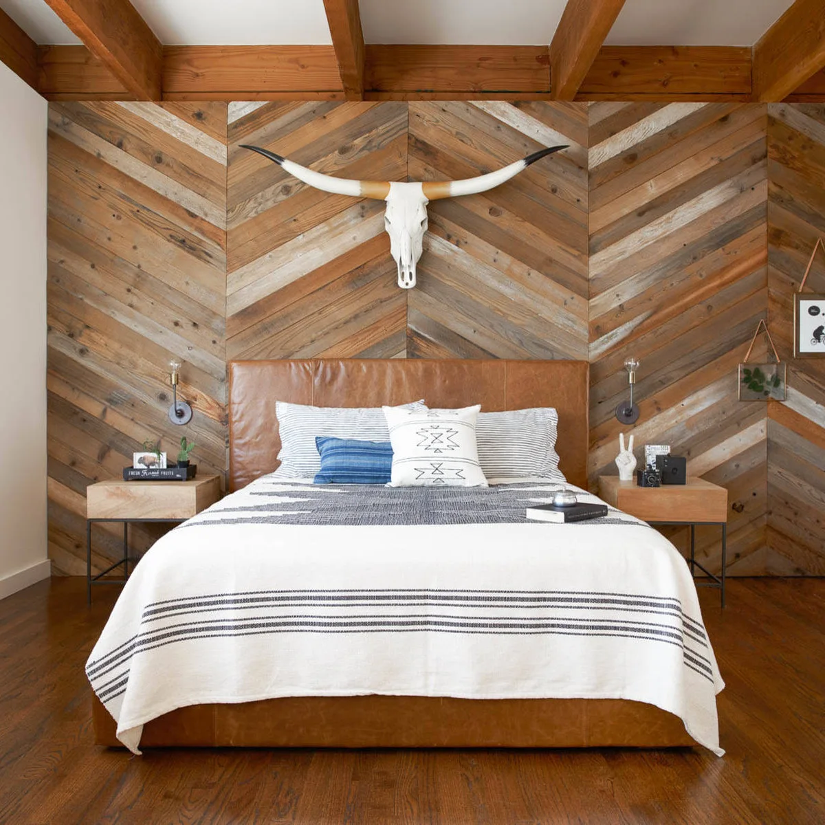 Bedroom with a tan upholstered bed, diagonal wood wall, longhorn skull display and black-and-white striped bedding