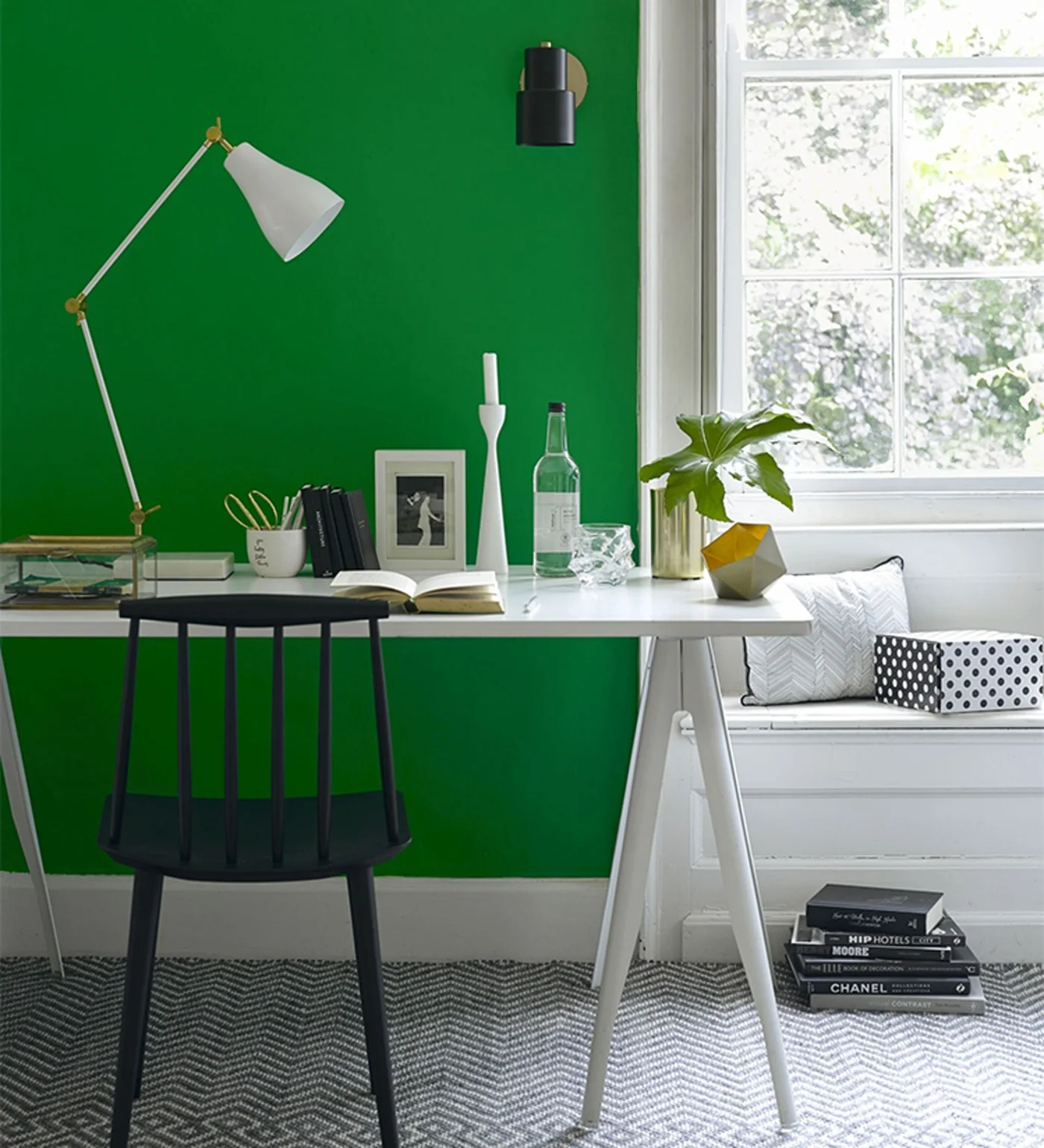 A bright green wall frames a pale desk and black chair beside a window seat and an adjustable pale task lamp