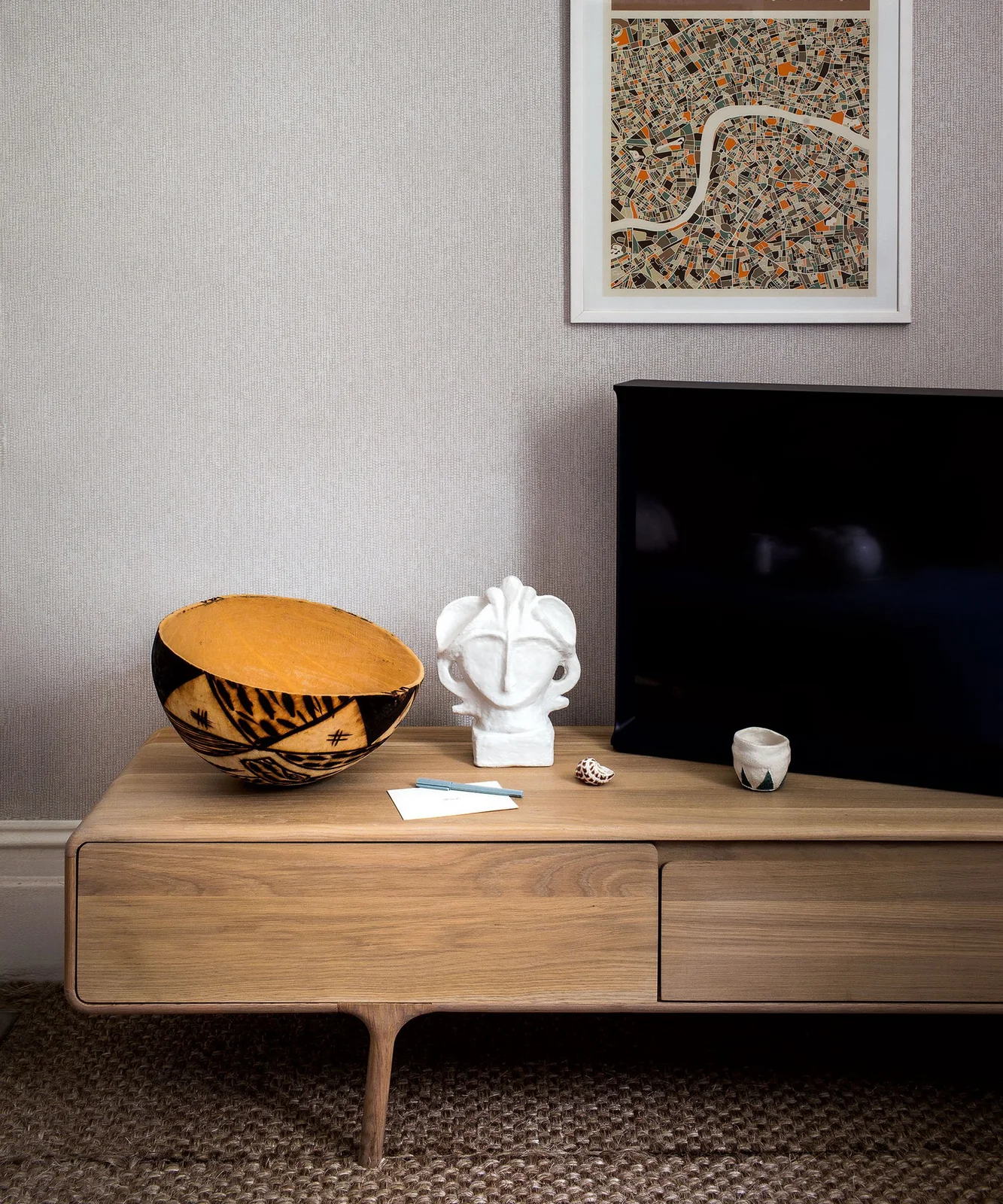 Wood-toned TV console with a decorative bowl, white sculpture and framed map above