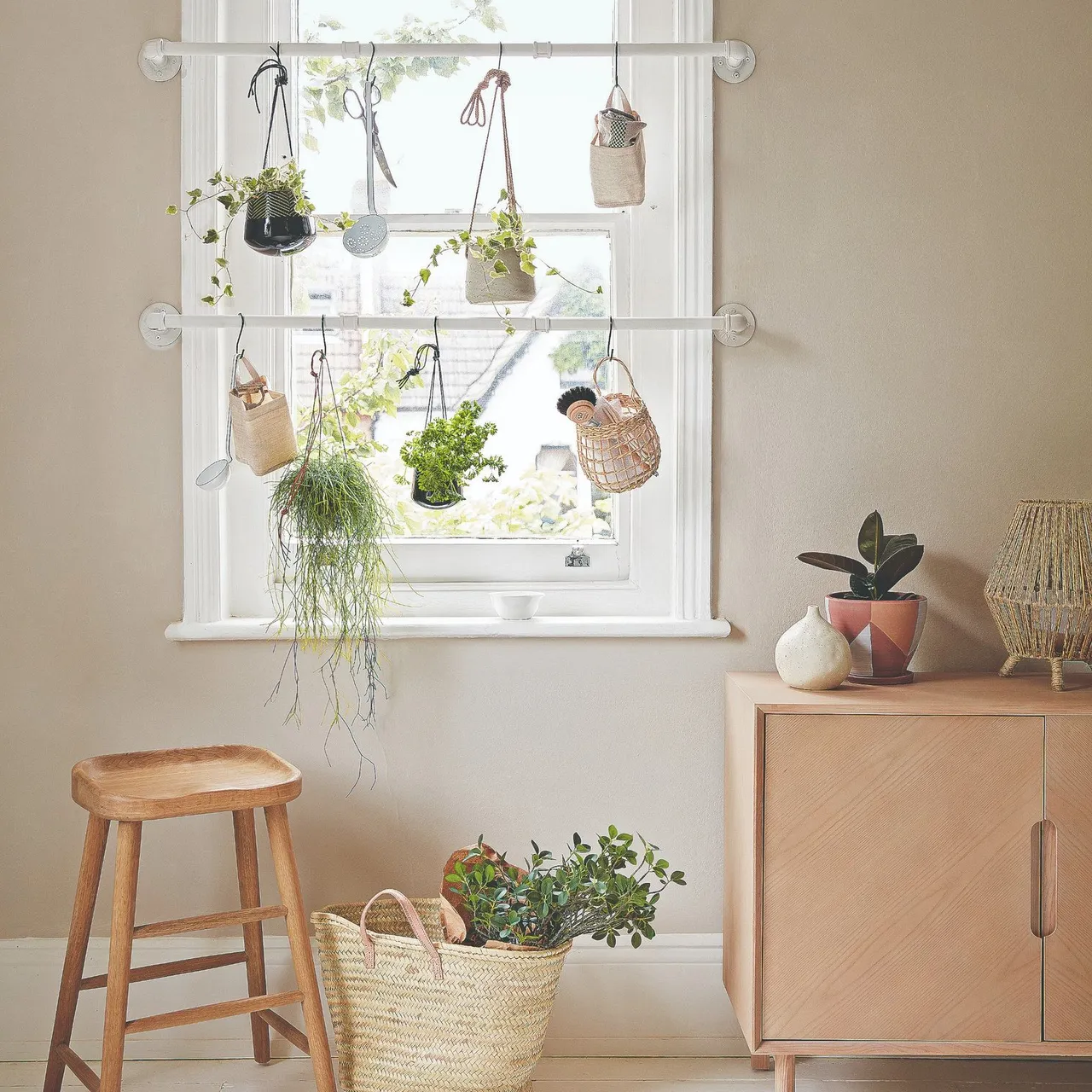 A pale timber cabinet sits beneath a bright window beside a stool and plants.