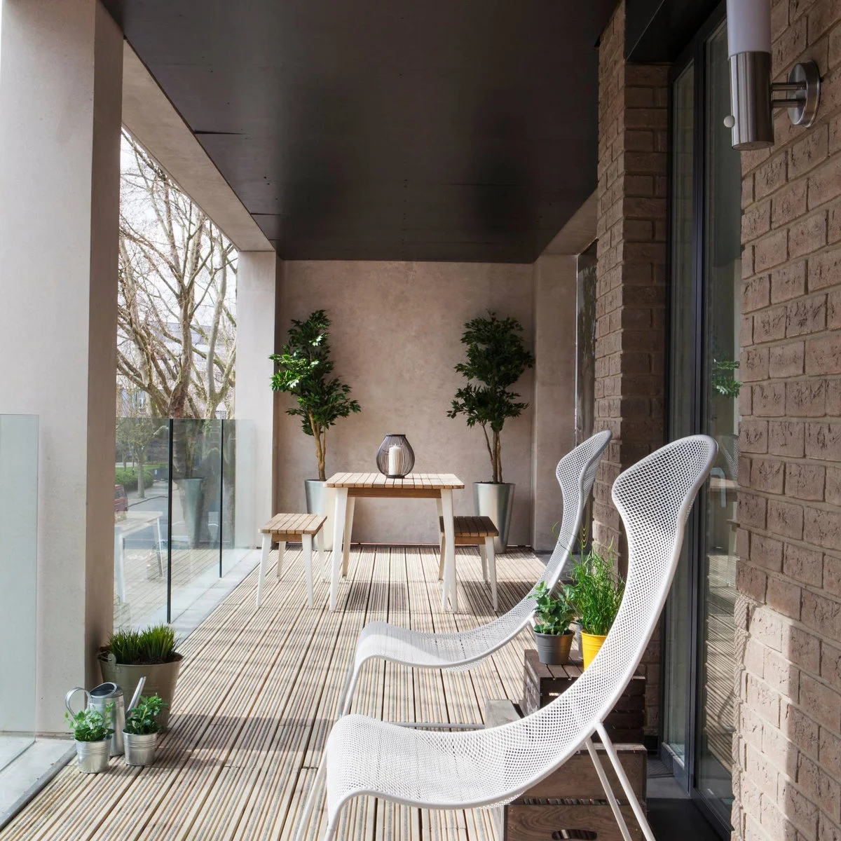 Long apartment balcony with two white lounge chairs and a small table with benches beyond