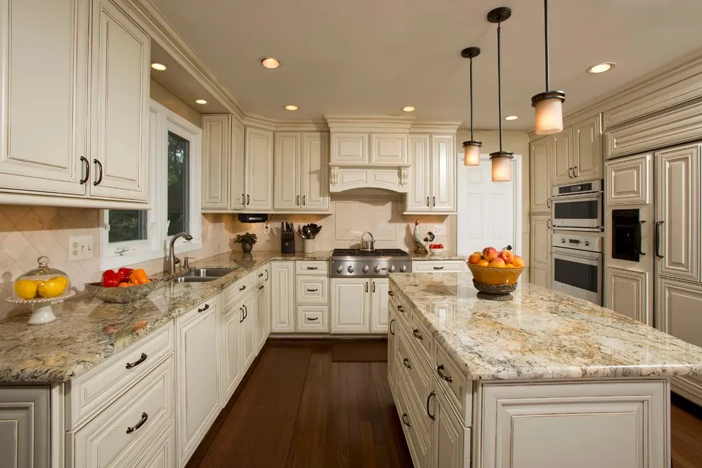 Cream paneled cabinets sit beneath a speckled stone counter in a long kitchen