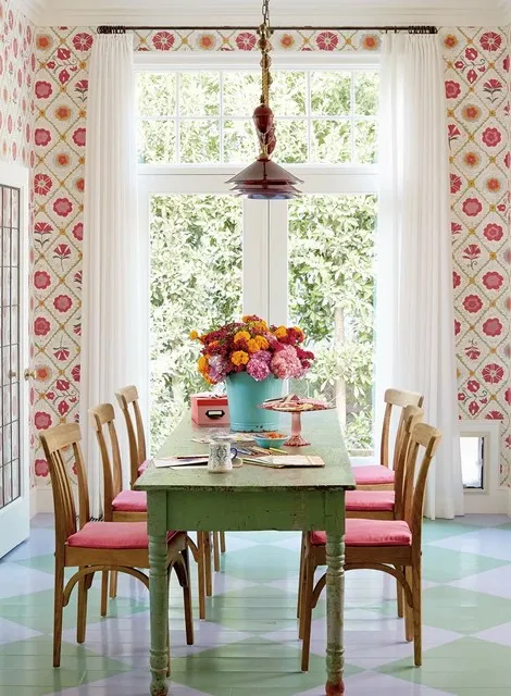 Pink patterned walls surround a green dining table beside a bright window.