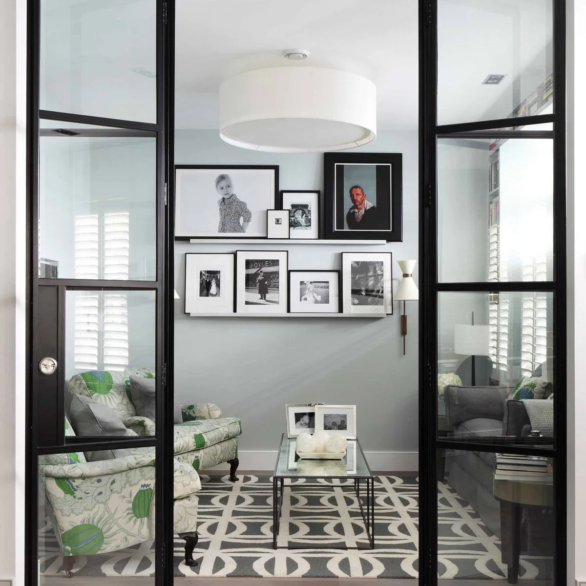 Small sitting room seen through black-framed glazed doors with pale walls and framed photographs
