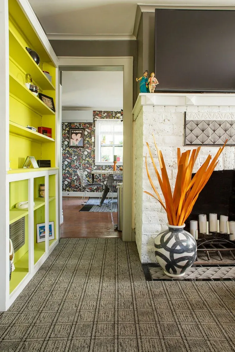 White-framed built-in with chartreuse shelf backs beside white brick fireplace and television