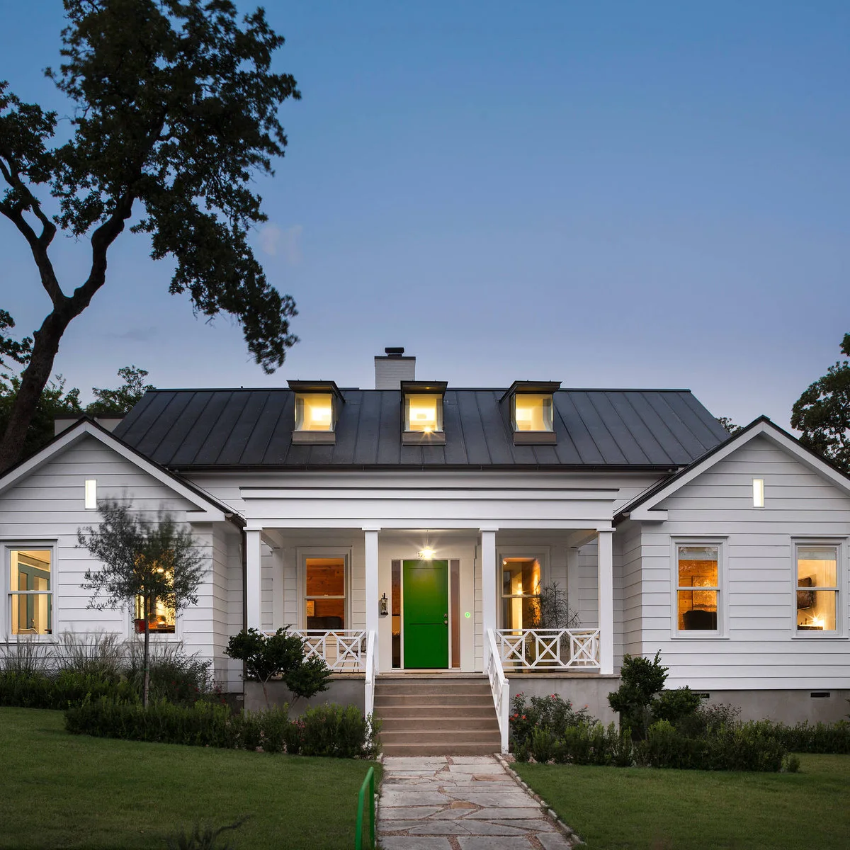 A white farmhouse with a green entrance door, broad concrete steps and low mixed planting beside the porch.