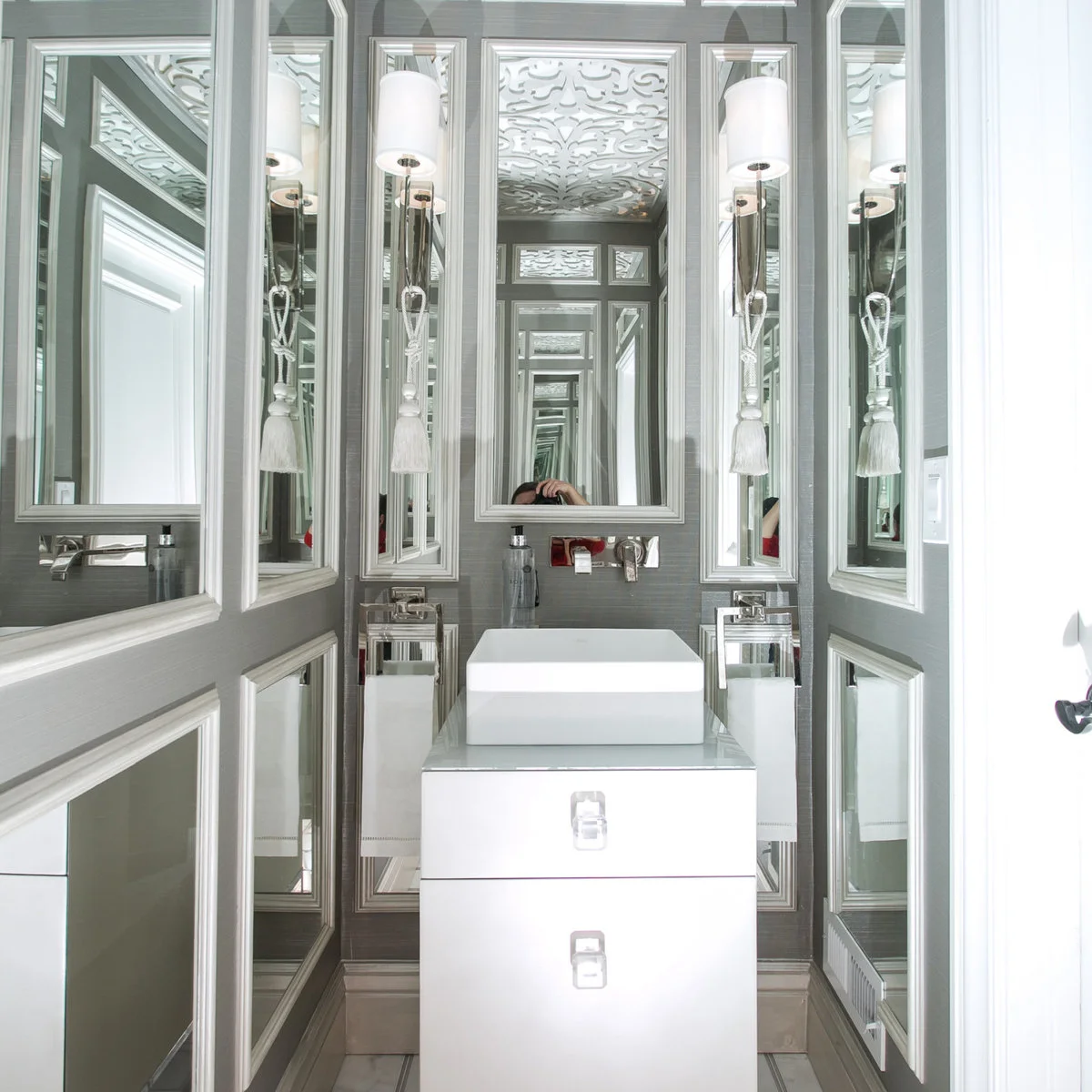 Narrow powder room with many white-framed mirrors and wall lights