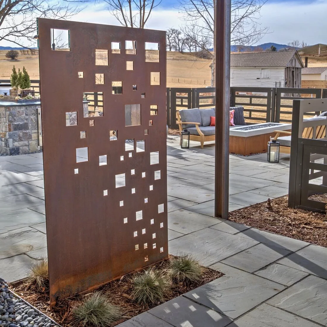 A reddish metal garden panel with square cutouts stands beside a paved patio
