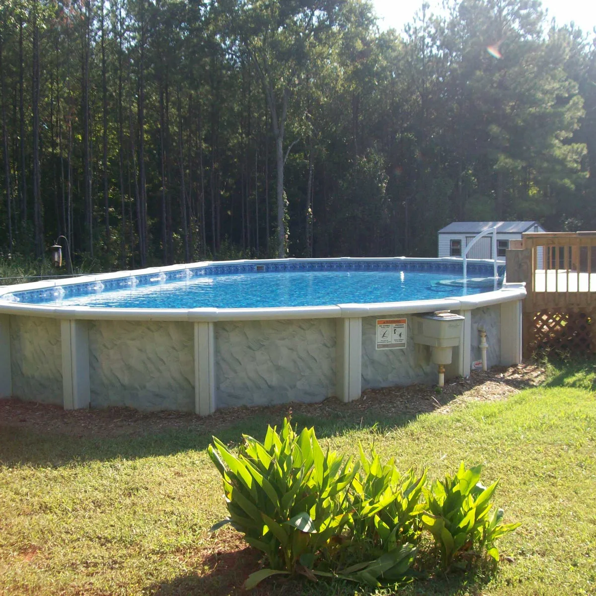 Oval above-ground pool with a short wood access deck at one end and low planting separated from the exposed wall.
