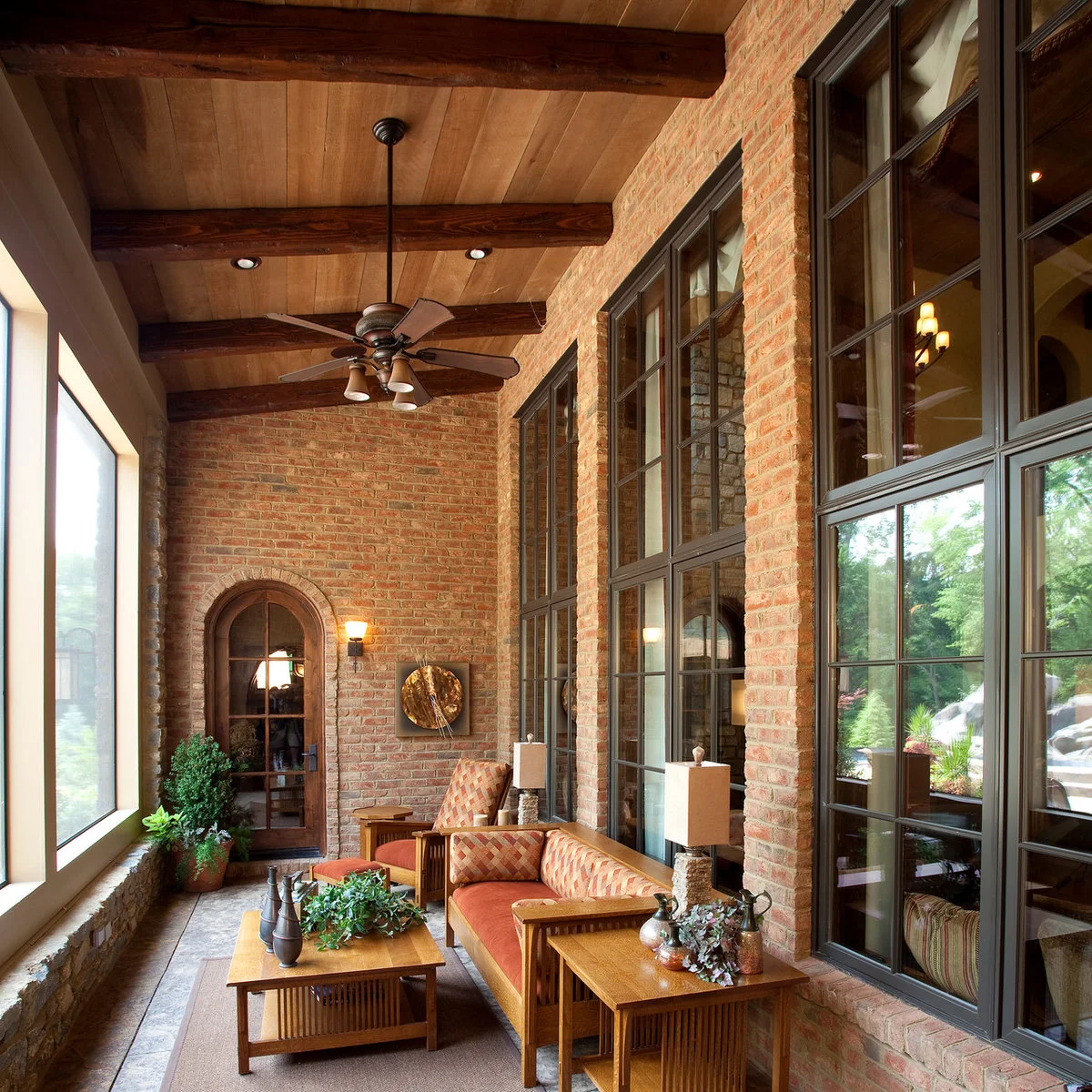 A long brick-walled porch with tall dark-framed windows, orange-cushioned wood seating and a wood ceiling.