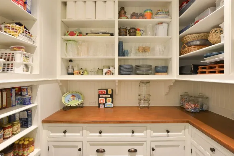 White country pantry with open shelves, brown counter, lower cupboards, dishes and stored groceries