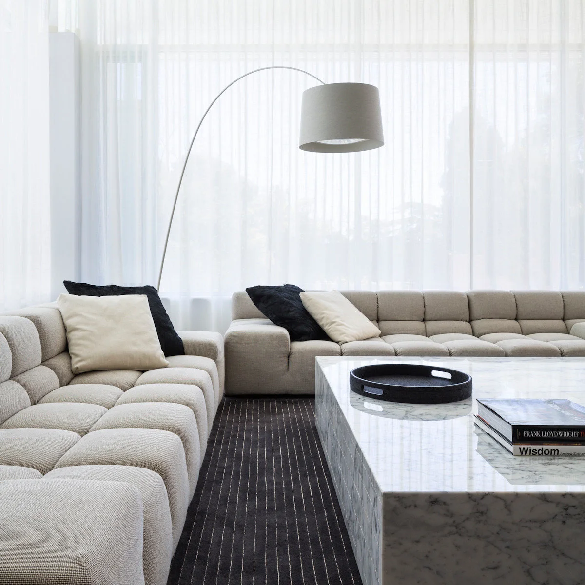 Pale tufted seating around a light table above a dark fine-striped rug