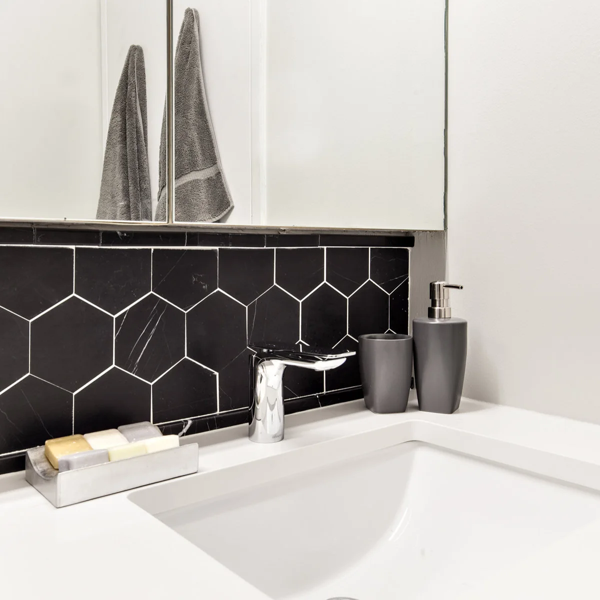 Short black hexagonal tile backsplash beneath a mirrored cabinet above a white basin and chrome faucet.