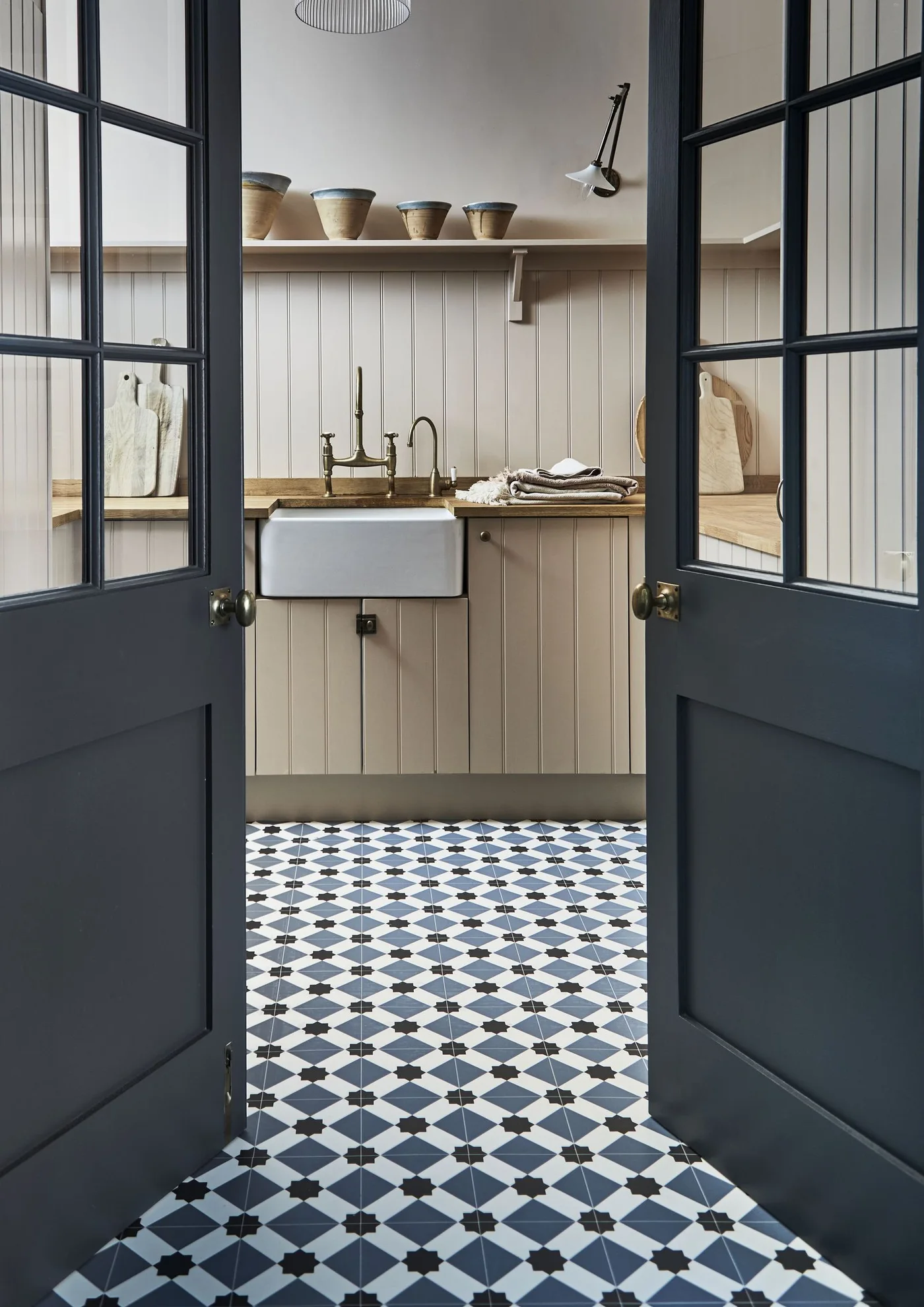 Cream boarded kitchen cupboards and wall with a wooden counter, apron-front sink, dark glazed doors and blue patterned floor.
