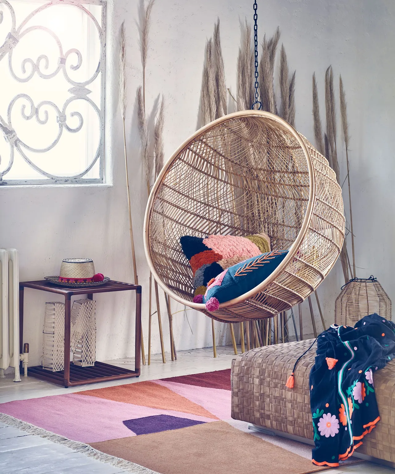 A rounded woven chair hangs beside a small cabinet in a pale room.